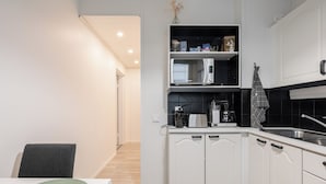 A modern kitchen with white cabinetry, a microwave, a coffee maker, and a sink.