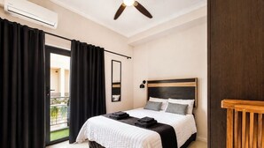 Een slaapkamer met een bed, zwarte gordijnen, een plafondventilator, een raam en een balkon.
