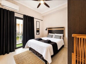 A bedroom with a bed, black curtains, a ceiling fan, a window, and a balcony.