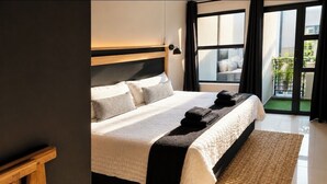 Een moderne slaapkamer met een groot bed, een houten hoofdbord, een geweven vloerkleed en uitzicht op het landschap door een groot raam.