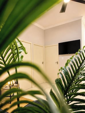 A room with a closed door, a flat-screen TV mounted on the wall, and a small table with a lamp.