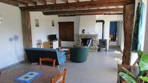 A living room with a fireplace, wooden beams, a television, and a dining area with a table and chairs. - Gîte in the heart of Suisse Normande  (Saint-Pierre-du-Regard)