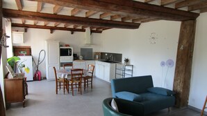 A living room with a green sofa, wooden dining table, and chairs, a kitchen with white cabinets, and a ceiling with exposed wooden beams. - Gîte in the heart of Suisse Normande  (Saint-Pierre-du-Regard)