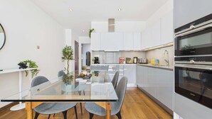 Une cuisine moderne avec des meubles blancs, une table à manger en verre et deux chaises grises.
