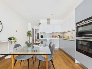 A modern kitchen with white cabinets, a glass dining table, and two grey chairs.