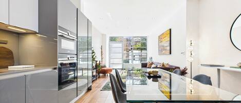 A modern kitchen with a glass dining table, wooden flooring, and a view of the outdoors.