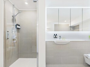 A modern bathroom with a glass-enclosed shower, a white sink with a mirror above it, and a toilet visible to the right.