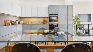 Une cuisine moderne avec des meubles blancs, une table à manger en verre et un four encastré.