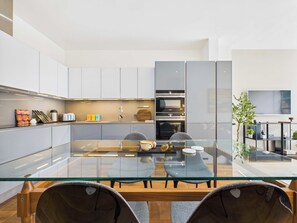 A modern kitchen with white cabinets, a glass dining table, and a built-in oven.