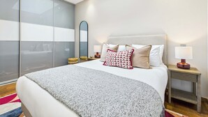 Une chambre à coucher moderne avec une lucarne, un grand lit agrémenté d’oreillers à motifs, des tables de chevet avec des lampes et un grand miroir.