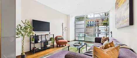 Una sala de estar moderna con un sofá grande, un televisor de pantalla plana, una mesa de centro de vidrio y una planta en maceta.