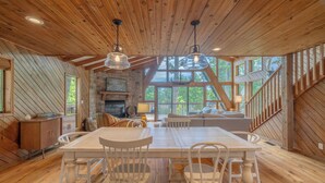 A spacious wooden interior with a dining area, stone fireplace, and large windows offering views of the outdoors. - Kitzbuhl Nook by Innsbrook Vacations! (Innsbrook)