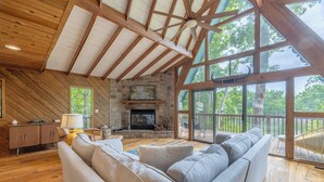 A spacious living room with a stone fireplace, wooden beams, and large windows overlooking a deck. - Kitzbuhl Nook by Innsbrook Vacations! (Innsbrook)