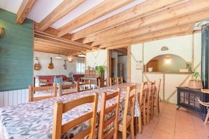 A dining area with wooden tables and chairs, a kitchen area with a stove, and a wooden ceiling structure.