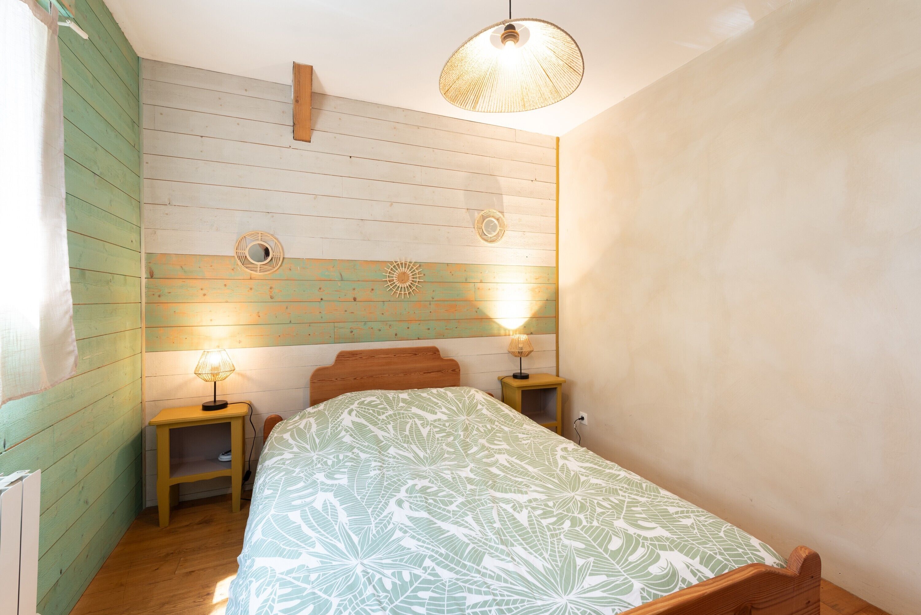 Une chambre à coucher comprenant un lit, deux tables de chevet, un luminaire suspendu et un mur orné d’un panneau en bois.