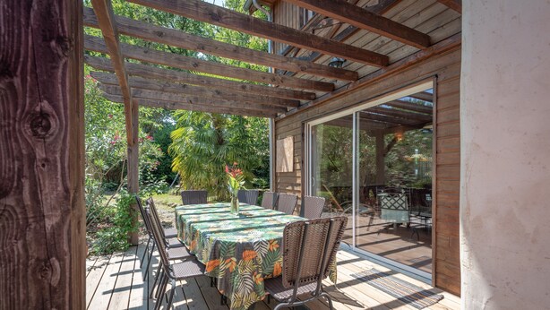 A covered outdoor patio with a table and chairs, surrounded by glass doors and wooden beams.