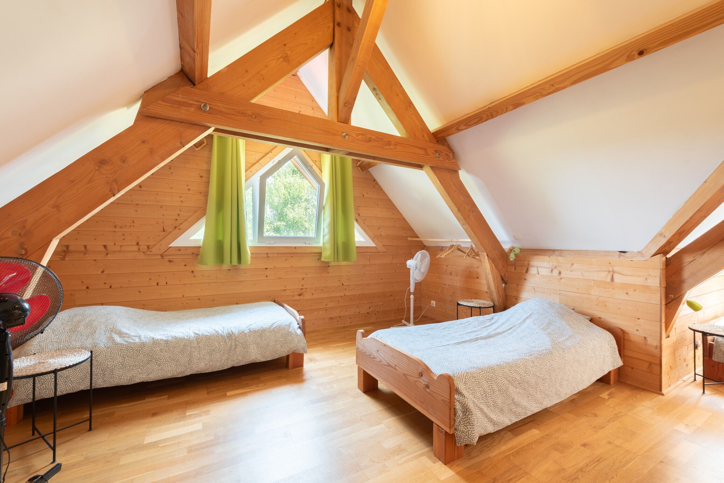 Une chambre aménagée en mezzanine avec deux lits en bois, un ventilateur et une fenêtre avec des rideaux.