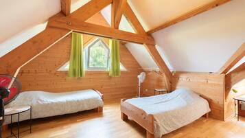 Une chambre aménagée en mezzanine avec deux lits en bois, un ventilateur et une fenêtre avec des rideaux.