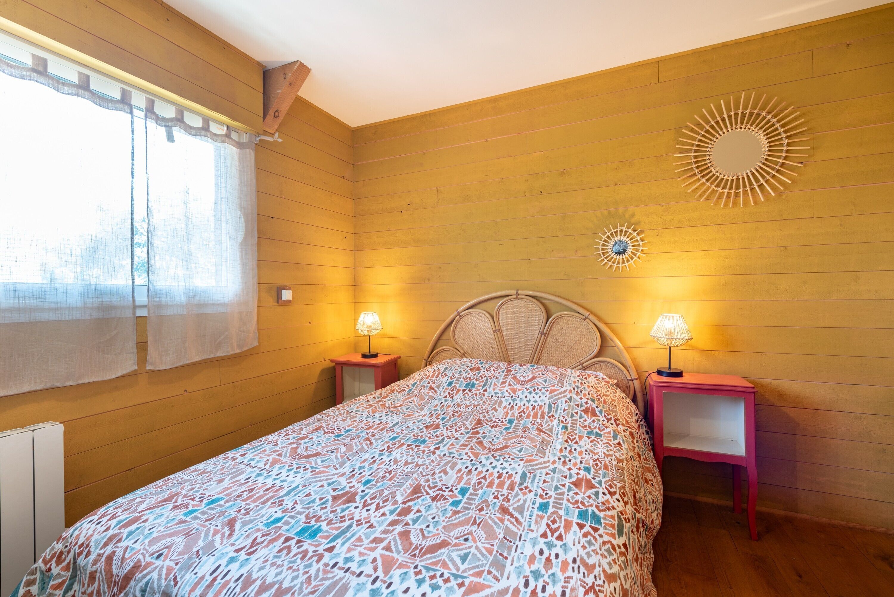 Una camera da letto con un letto, due comodini con lampade, una finestra con tende e un oggetto decorativo a parete.