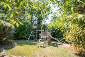 A wooden playhouse with a slide and a swing set in a garden.