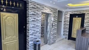 Um lobby moderno com entrada preta e dourada, parede estampada e uma pequena lixeira.