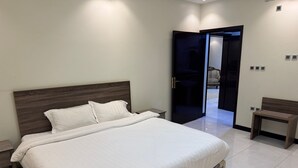 Quarto moderno com uma cama grande, mesas de cabeceira, um banco e uma porta que dá para outro cômodo.