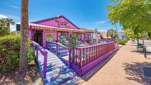 A brightly colored building with a sign reading "The Fudge Factory," featuring a purple exterior and a staircase leading to the entrance.