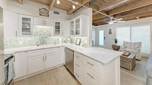 A modern kitchen with white cabinetry, a marble countertop, and a wooden ceiling.