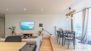 A modern living room with a flat-screen TV, a dining area with a table and chairs, and a large window with curtains. - L'Ovalino: Quiet, 100m² T4 apartment (Montpellier)