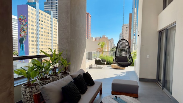 Een balkon met een bank, voetenbankje, hangstoel en potplanten.