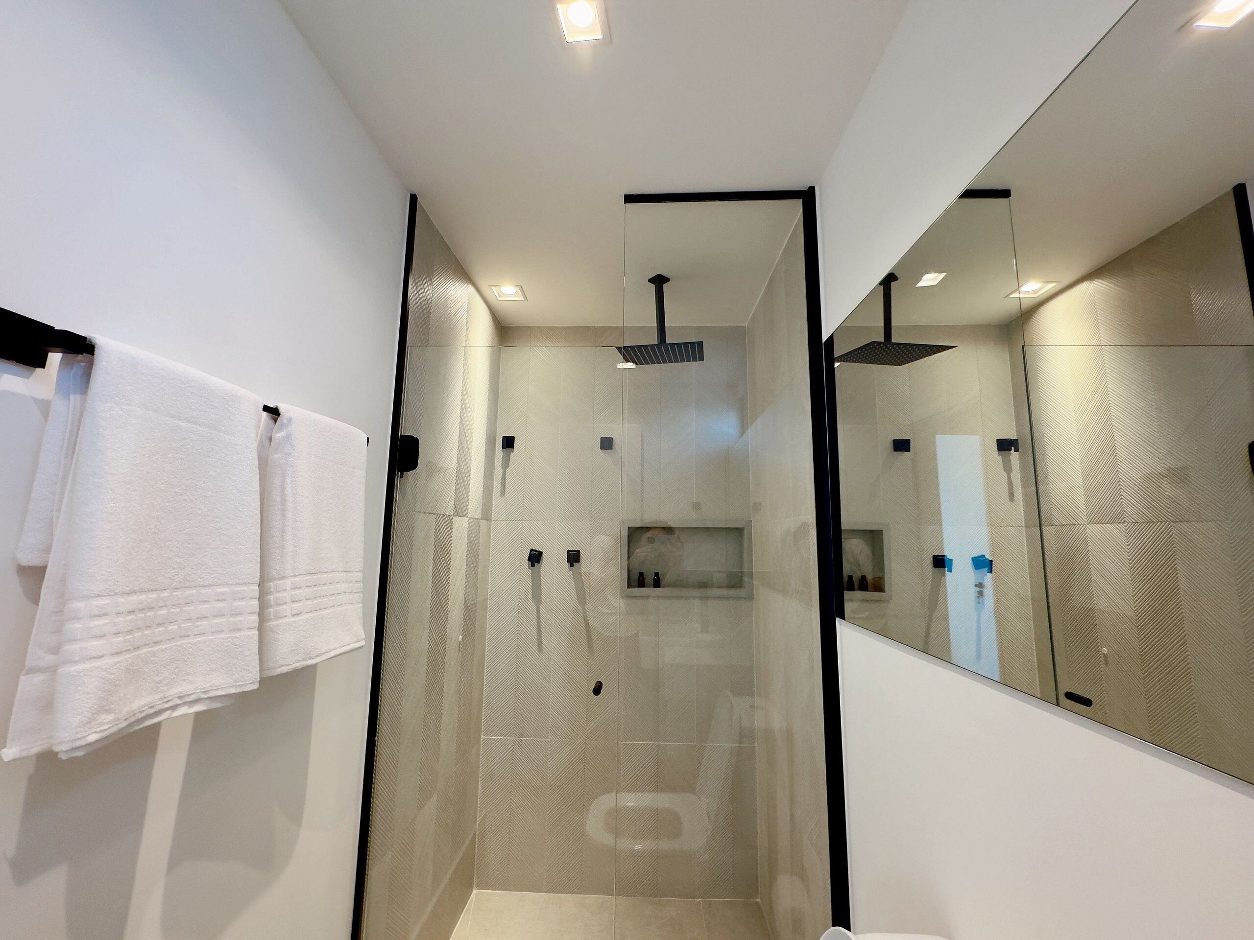 A modern bathroom with a glass-enclosed shower, a large mirror, and white towels on a rack.