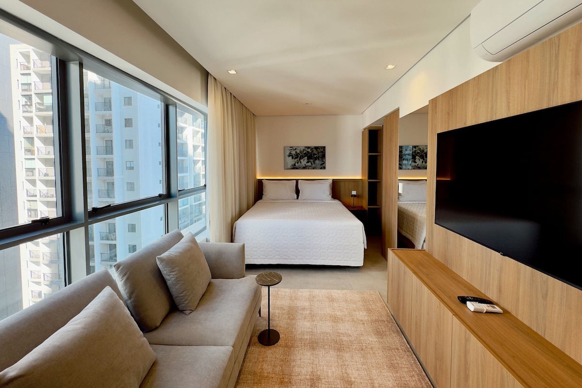 Une chambre d’hôtel moderne dotée d’un grand lit, d’un canapé, d’une télévision et offrant une vue sur la ville.