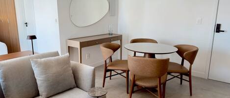 A modern living room with a sofa, a coffee table, and a dining area with chairs and a table.