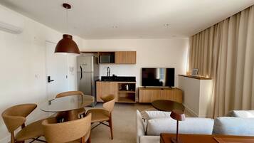 A modern living room with a glass dining table, beige sofas, and a flat-screen TV.