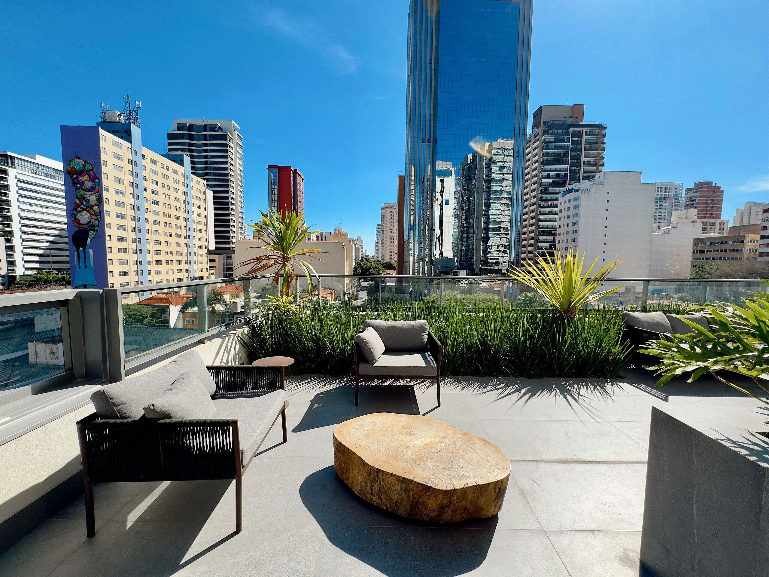 Una terraza en la azotea con mobiliario exterior, vistas del horizonte urbano y un mural grande en el edificio.