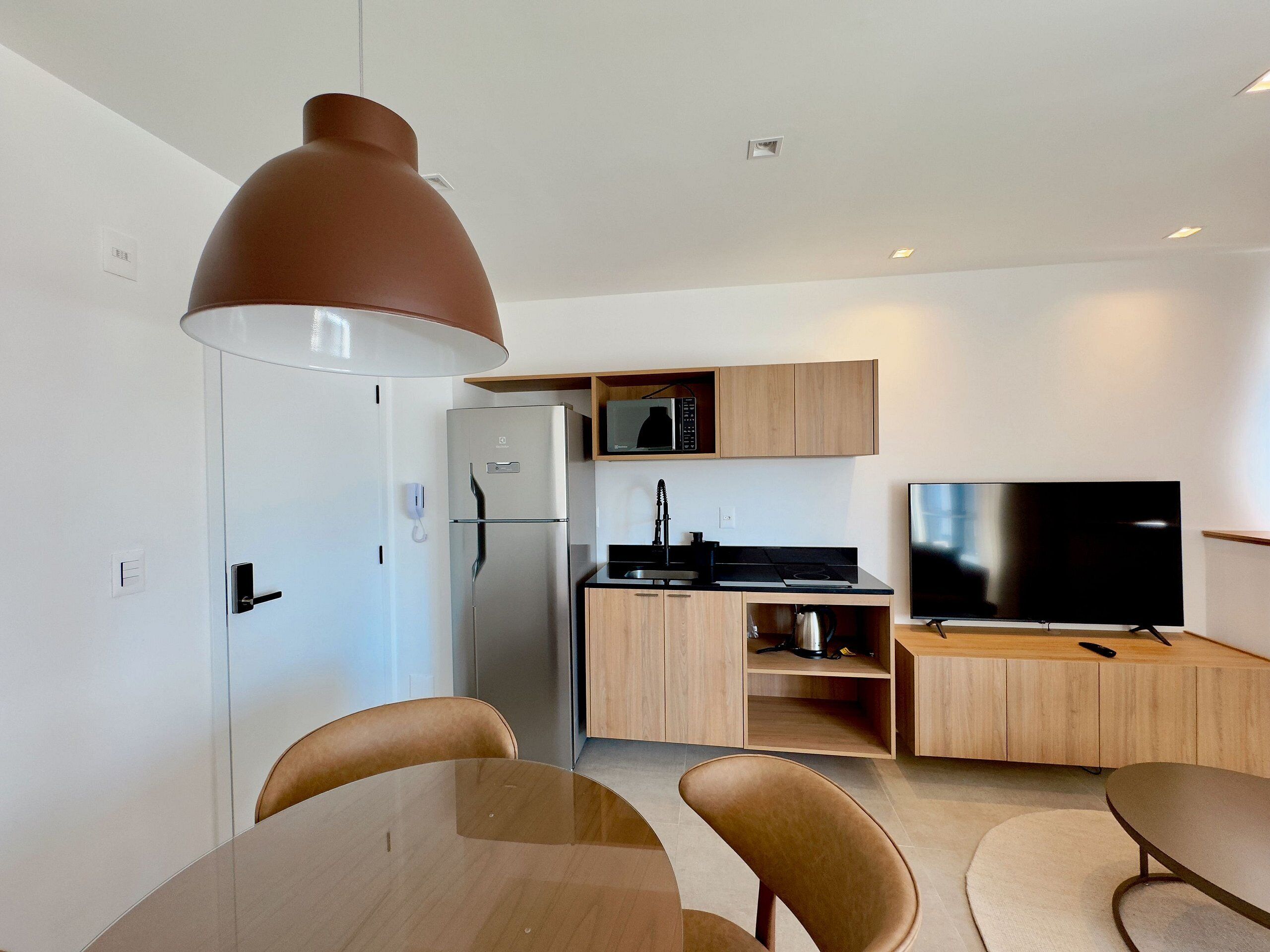 A modern kitchen with a refrigerator, microwave, and stove, a dining area with a table and chairs, and a flat-screen TV.