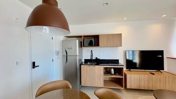 A modern kitchen with a refrigerator, microwave, and stove, a dining area with a table and chairs, and a flat-screen TV.