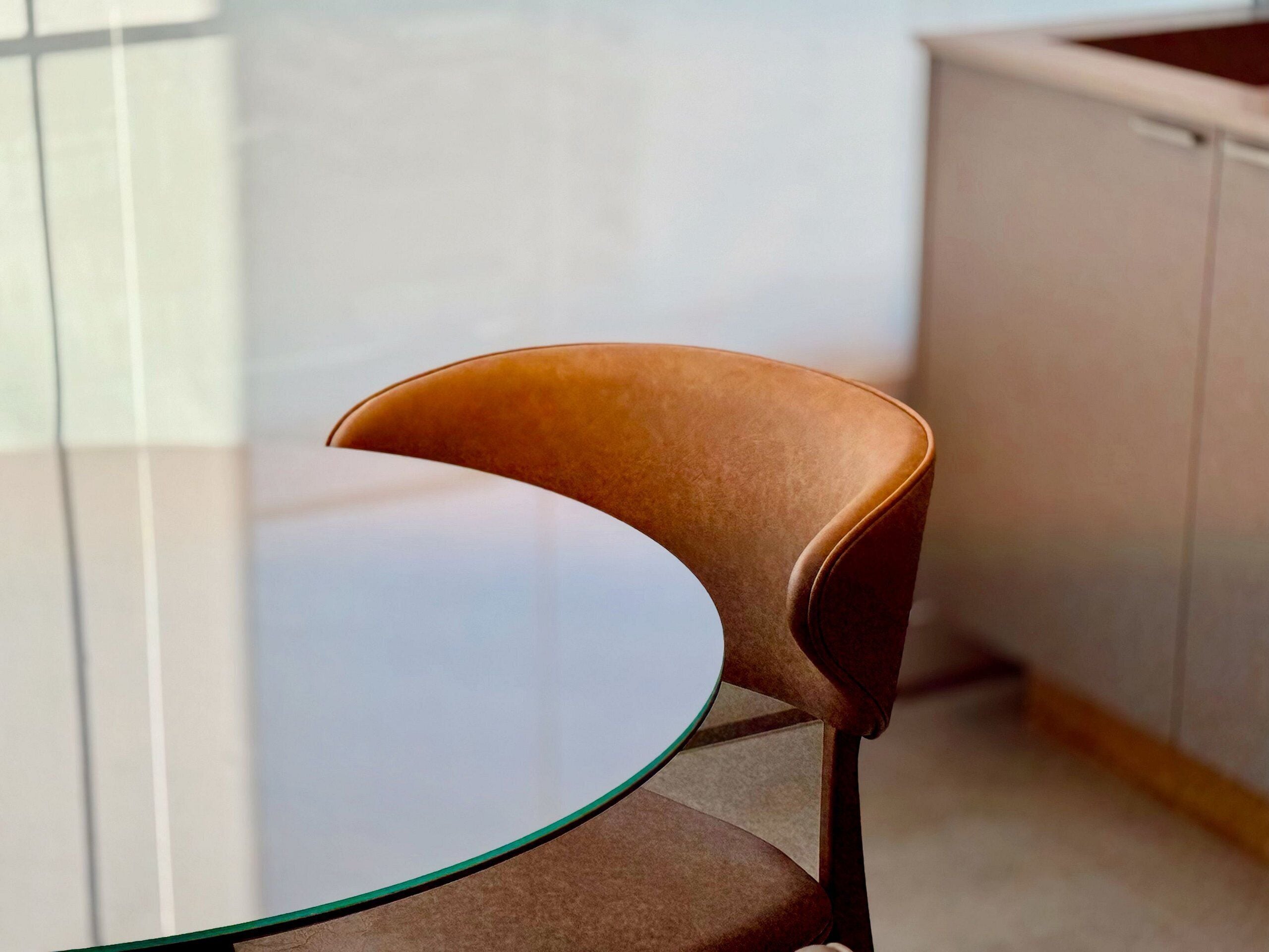 A modern chair with a curved backrest and metal legs, positioned at a glass table in a room with a tiled floor and a light-colored cabinet in the background.