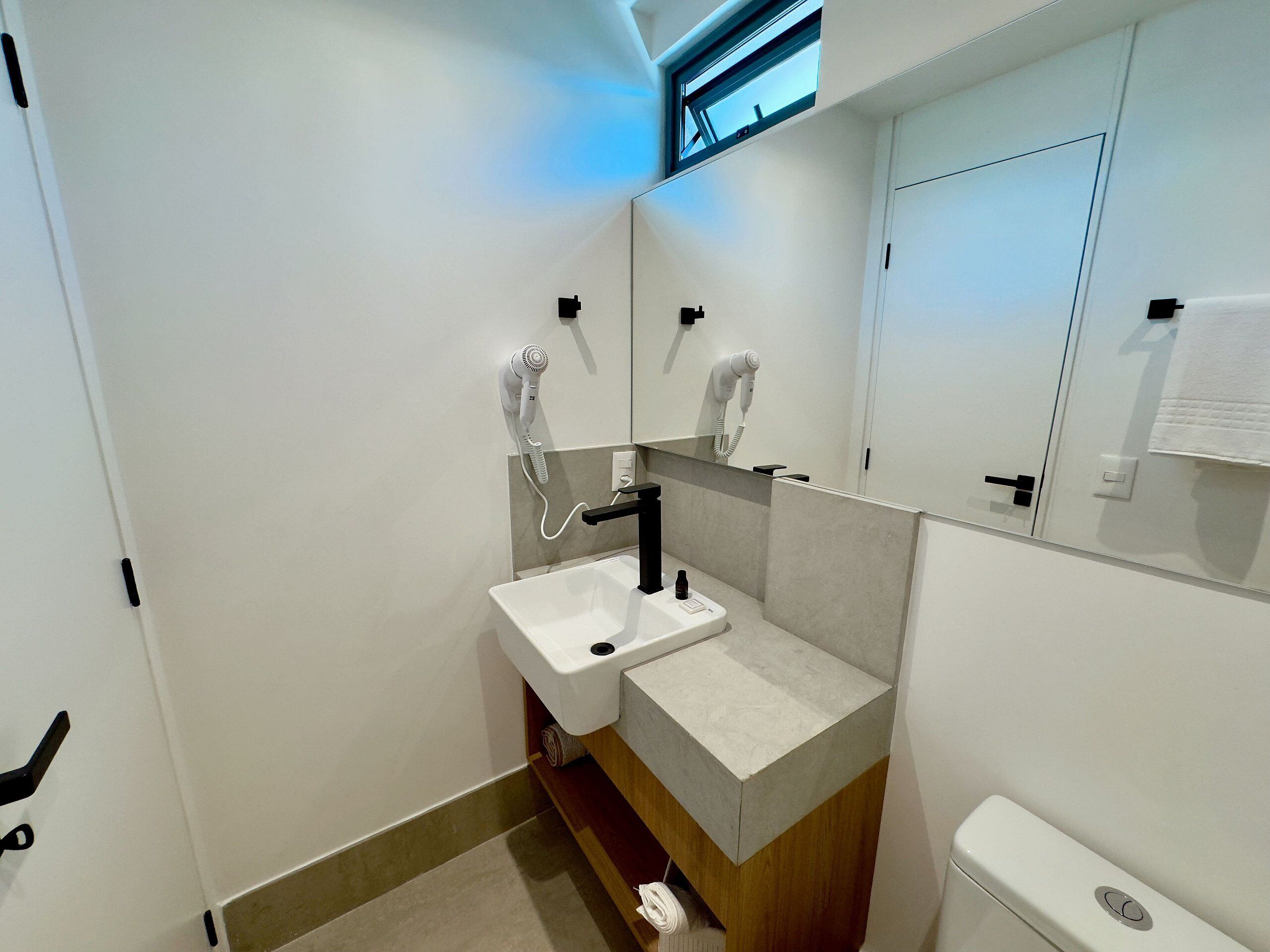 A modern bathroom with a white sink, a hairdryer mounted on the wall, and a toilet.