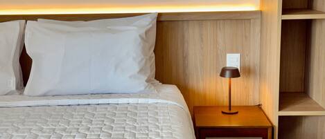 A neatly made bed with white bedding, a bedside lamp, and a wooden nightstand.