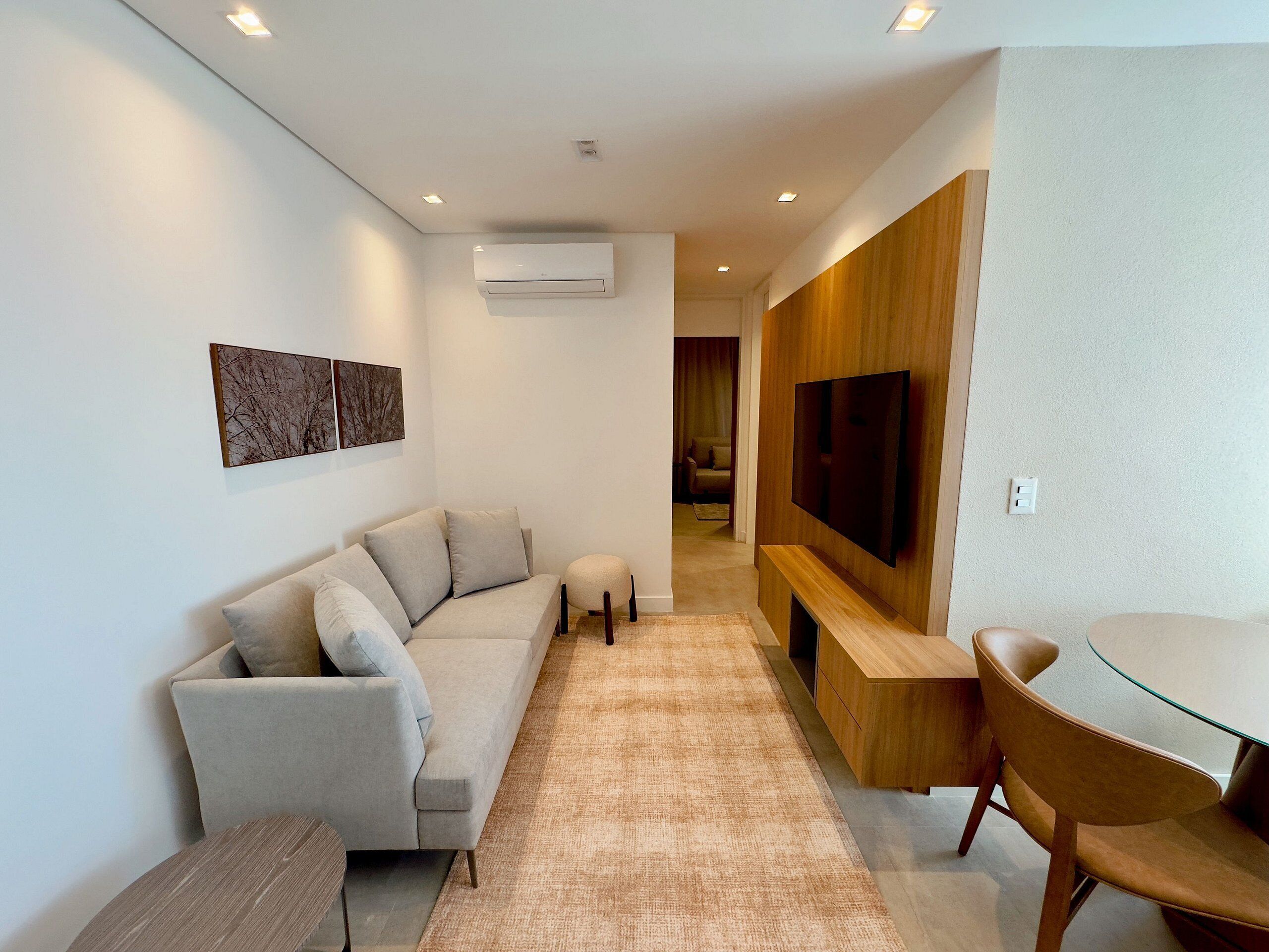 Una sala de estar moderna con un sofá, una mesa de centro, un televisor montado en una pared de madera y un comedor con una mesa de vidrio y sillas.