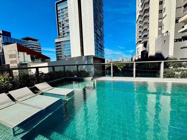 A rooftop pool with clear blue water, surrounded by modern buildings and a glass balustrade. - Homm Pinheiros (Sao Paulo)