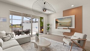 A modern living room with a sofa, coffee table, and chairs, a TV mounted on the wall, and a large window overlooking a balcony.