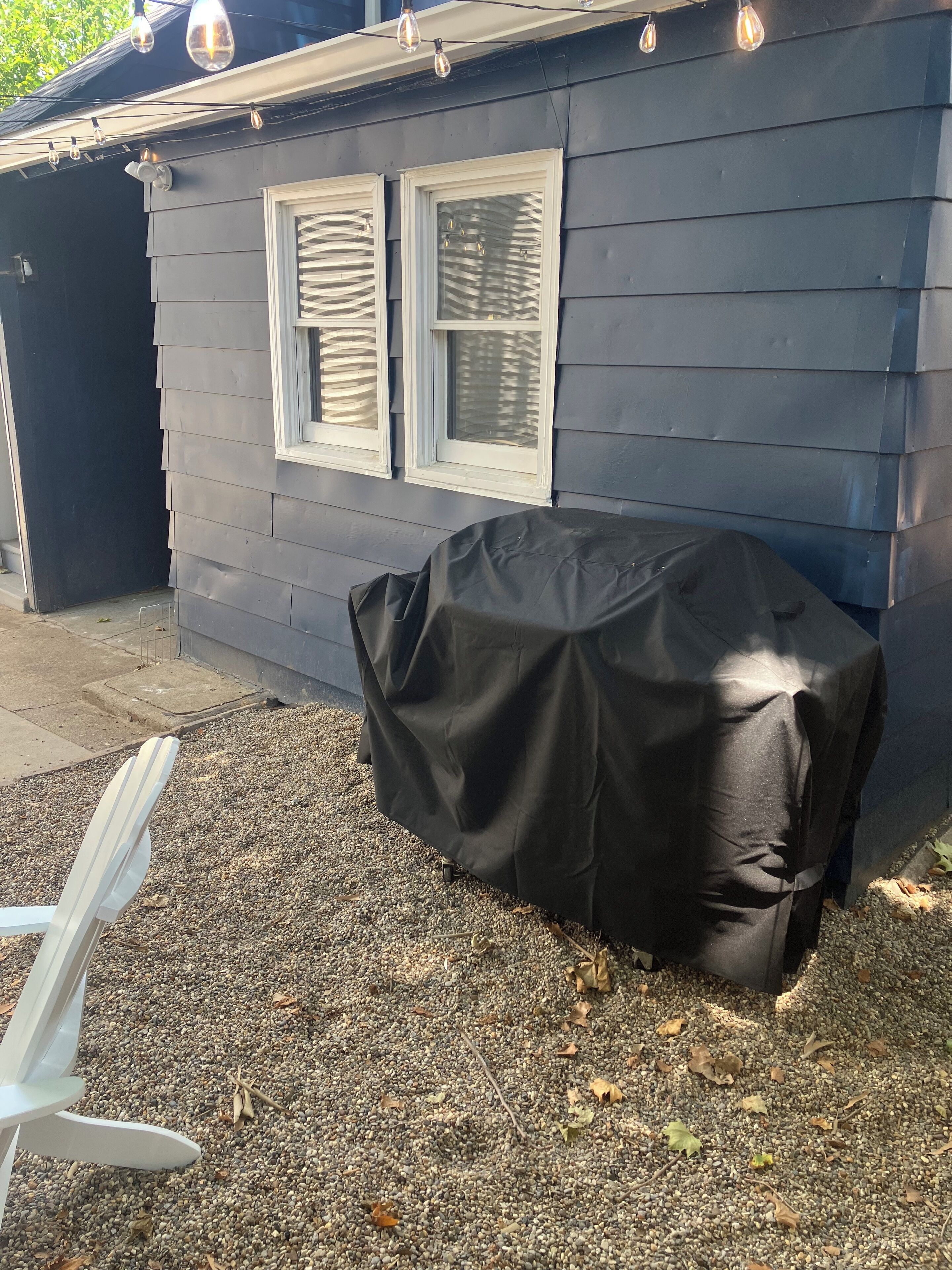 Una casa con una parrilla cubierta, una silla blanca y un camino de entrada de grava.