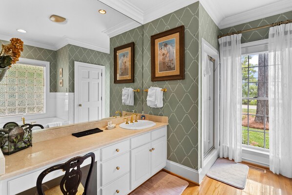 A bathroom with a large vanity, two framed pictures, a window with curtains, and a view of greenery outside. - Lake Escape - Lake Waccamaw 7 Bedroom Home (Lake Waccamaw)
