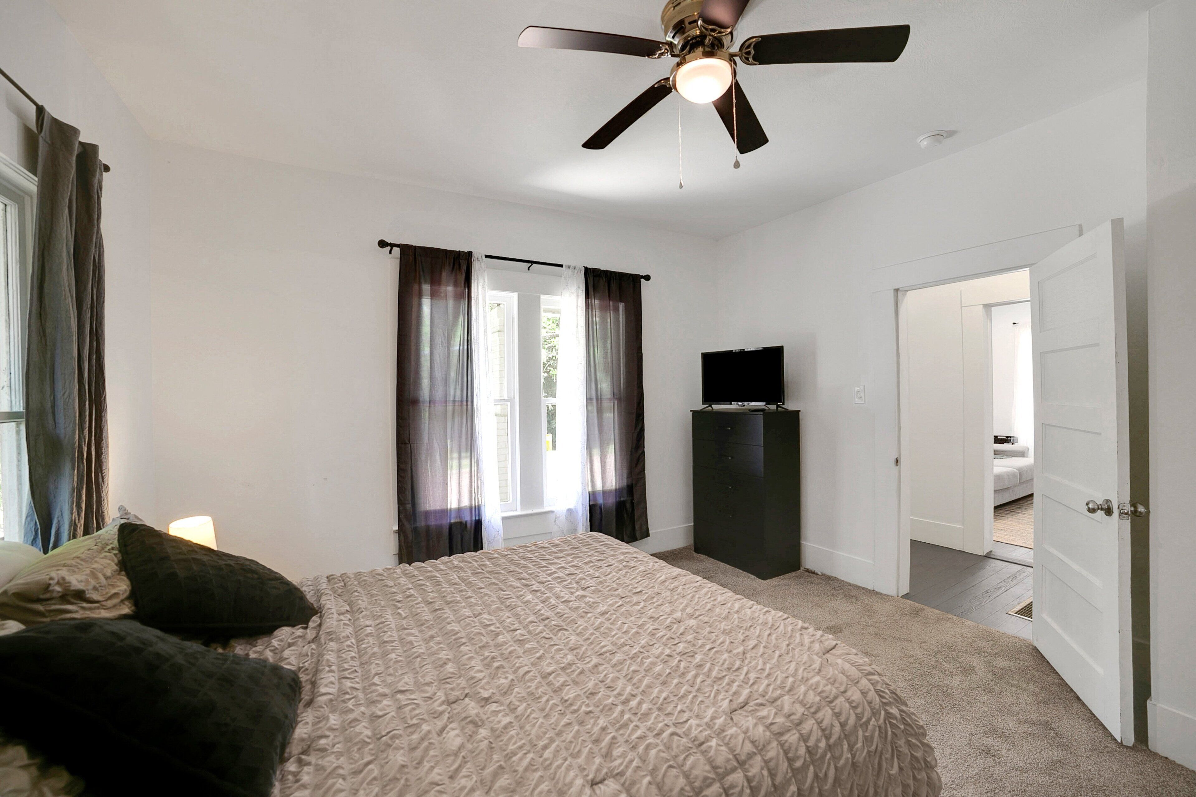 A bedroom with a bed, curtains, a ceiling fan, a television, and a wardrobe.