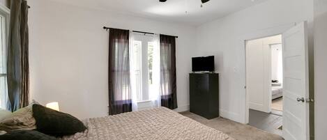 A bedroom with a bed, curtains, a ceiling fan, a television, and a wardrobe.