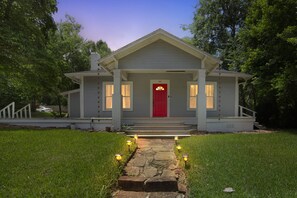 A single-story house with a red door, numbered 312, and a stone pathway leading to the front steps.