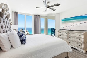 Camera da letto con un letto grande, una ventola a soffitto, un comò e un'ampia finestra con vista sull'oceano.