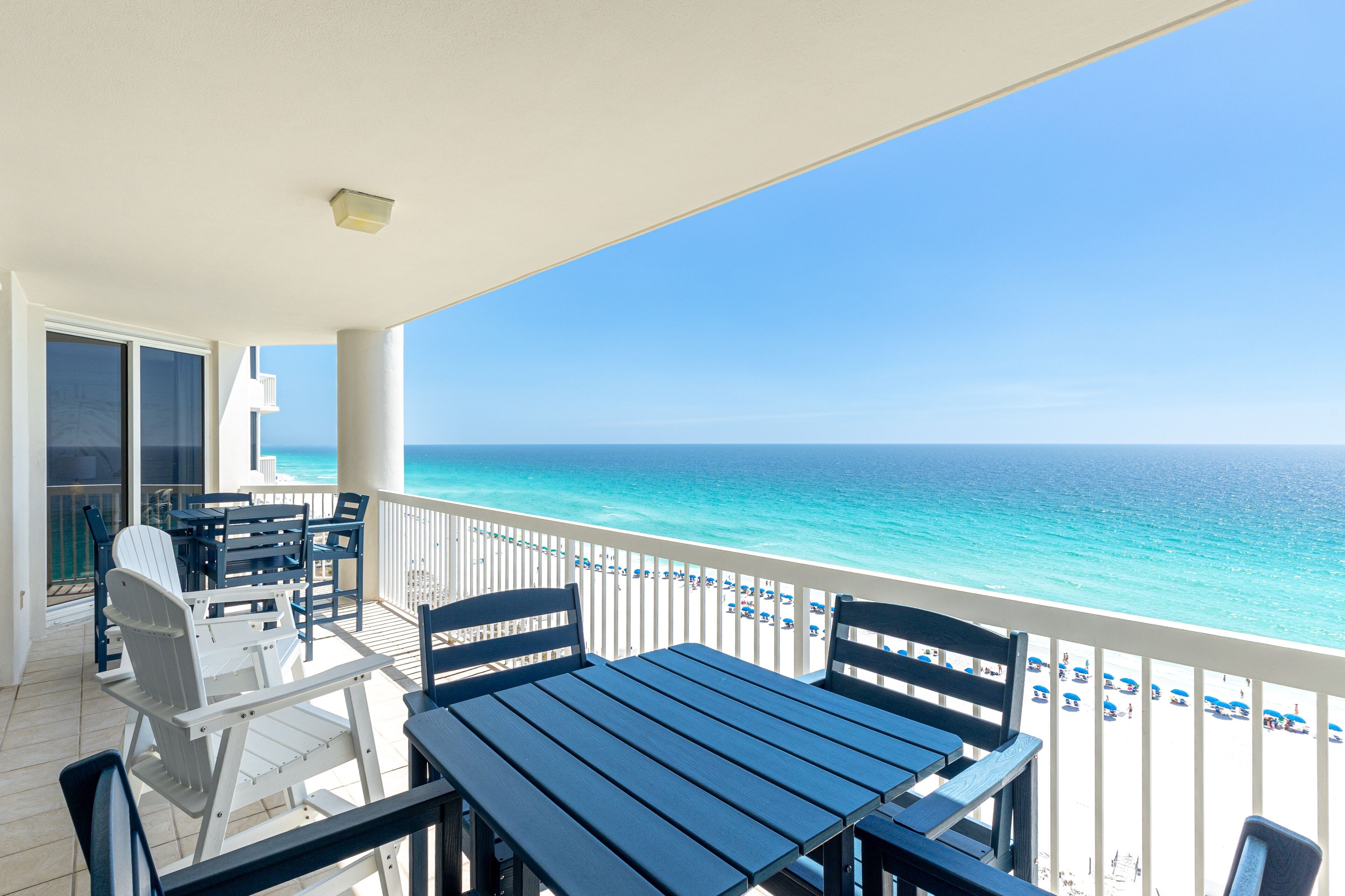 A balcony with a view of the ocean, a table and chairs, and a white railing.